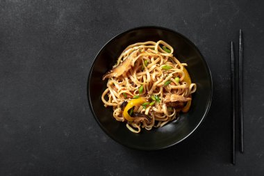 Arka planda bir kasede Asya eriştesi. Vejetaryen eriştesi, sebzeli erişte Hakka Eriştesi veya siyah bir kasede Chow Mein.
