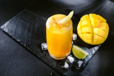 Siyah arka planda mango suyu. Buzlu, mango dilimli ve limonlu yaz içeceği. Mango ve limon suyu nektarı. Siyah arka planda ferahlatıcı bir yaz içkisi. Parlak sarı ve siyah renkler