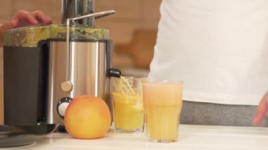 Erkeklerin elleri meyve sıkacağında hazırlanmış iki bardak taze meyve suyu alır. Greyfurt ve portakal suyu sağlıklı gıdalar, diyet için meyveler ve vücudun zehirlenmesinden arınmasıdır. Bir içki hazırlıyorum.