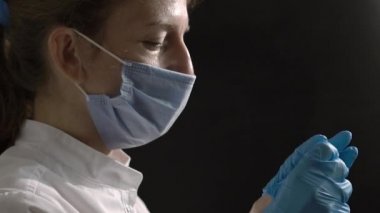 A female surgeon doctor or nurse, tired, takes off her protective medical gloves against a black background. Professional lighting in the frame. Concept work of doctors during the covid pandemic
