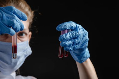 A female virologist works with blood tubes against a black background. A nurse is holding blood tubes in her hands. Concept of work on a pandemic vaccine.