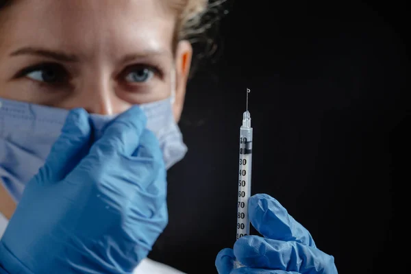 A tired doctor with a syringe on a black background. The doctor adjusts the mask on his nose