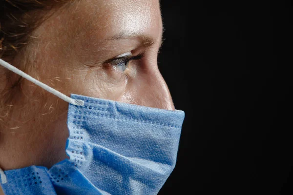 Portrait of a tired or sad depressed doctor in close-up on a black background. A dramatic portrait of a doctor. Doctor tired at work. Nurse in protective blue mask tired.