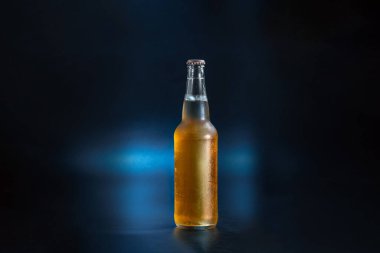 unlabeled bottle of lemonade on a dark blue background. The bottle of kambucha is fogged up. Cold bottle of fermented lemonade.