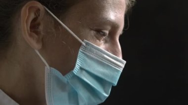 A distraught woman doctor or nurse against a dark background. The concept of a doctors hard work. Nurse on dark background crying from fatigue and stress. Woman in protective mask is upset. Omicron