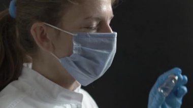 The doctor checks the drug and then slowly looks into the camera. The nurse at work checks the vaccine in the tube and looks into the camera against a black background. Tired doctor