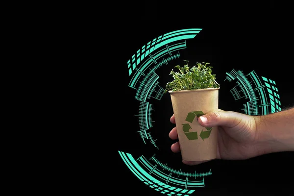 A mans hand holds an eco glass with a green plant on a black background. Blank space for text . Smart and modern recycling. Life without plastic. The concept of ecological technology. Sustainable