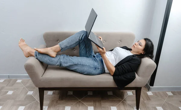 Happy calm female employee working at her laptop in the comfort of her couch. Work at home. Comfortable working at the computer