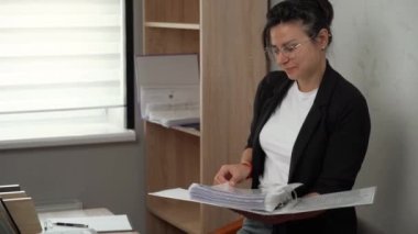A businesswoman looks at a binder of papers. Working with documents in the office.