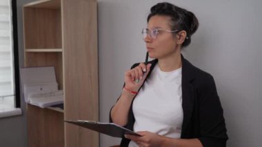 a young beautiful woman waved a pen, thoughtfully began to write something in the papers. The booghalter or manager in the office thinks and works.