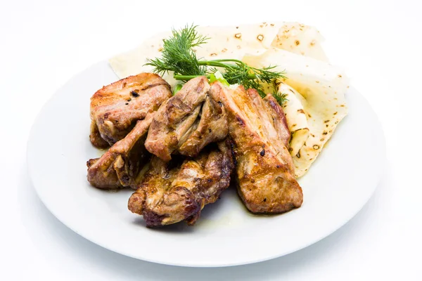 Izgarada kızarmış domuz kaburgası ve beyaz bir tabakta pide.