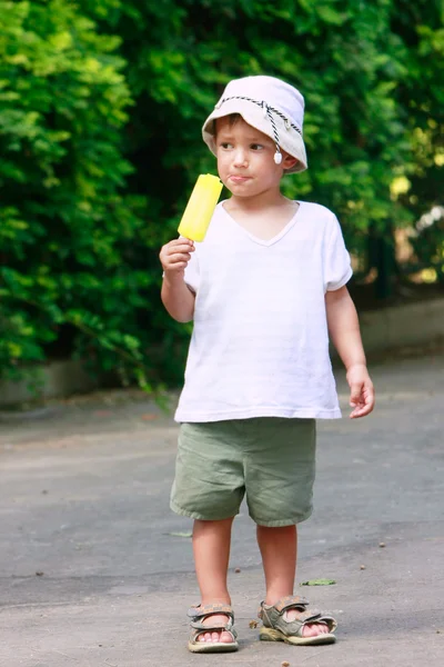 Young boy eating yellow ice-cream on natural background — Zdjęcie stockowe