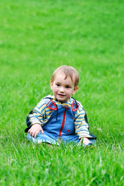 Young boy sitting in green grass — Zdjęcie stockowe