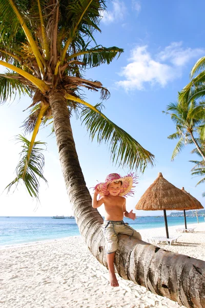 Lycklig pojke sitter på palm, sandstrand bakgrund — Stockfoto