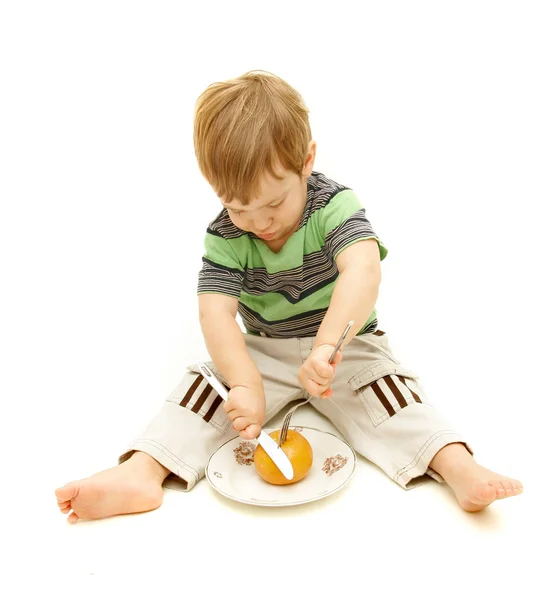 Niño cortando naranja con tenedor y cuchillo sobre blanco — Foto de Stock