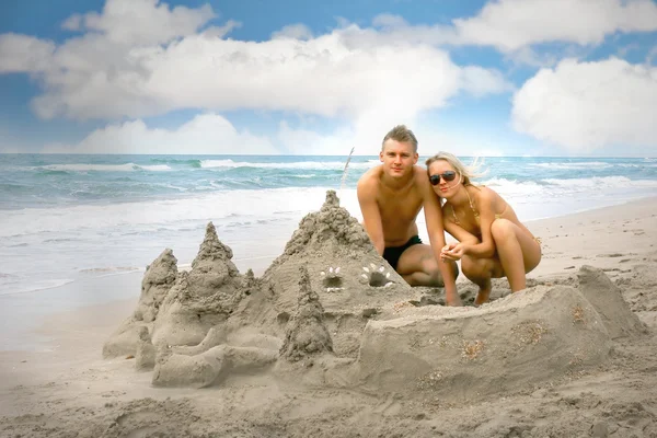 Giovane coppia vicino castello di sabbia sulla spiaggia — Foto Stock