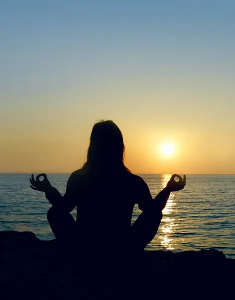 Женский силуэт, делающий йогу на фоне заката моря — стоковое фото