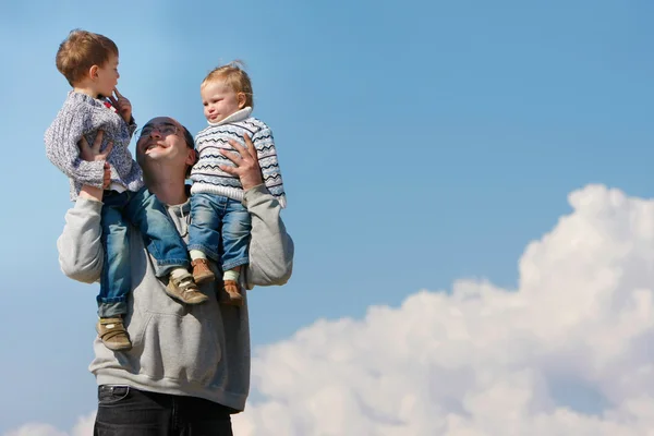 Πατέρας των δύο παιδιών εκμετάλλευση στους ώμους του πάνω από το φόντο του ουρανού — Φωτογραφία Αρχείου