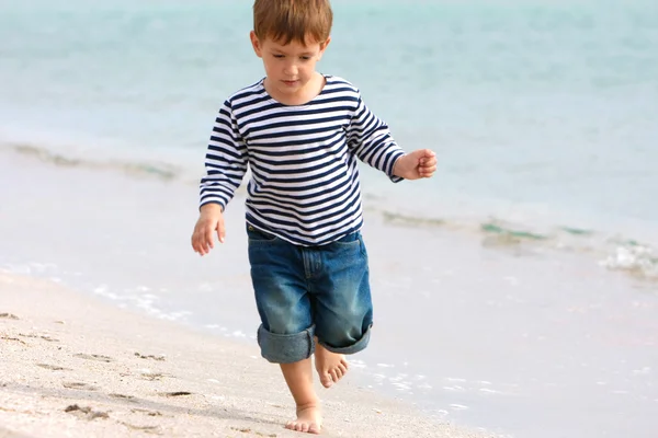 Söt pojke går på sandstrand — Stockfoto