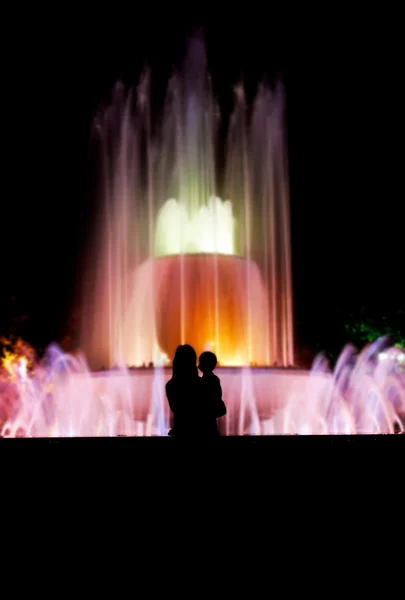 Силуэт матери и ребенка на красочном фоне фонтана — стоковое фото