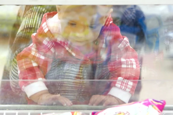 Niño mirando a través de la ventana de vidrio en el supermercado — Foto de Stock