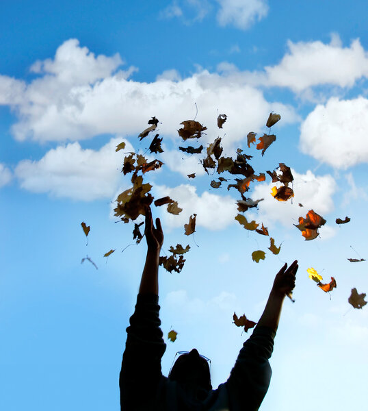 silhouette of man throwing up autmn leaves over sky