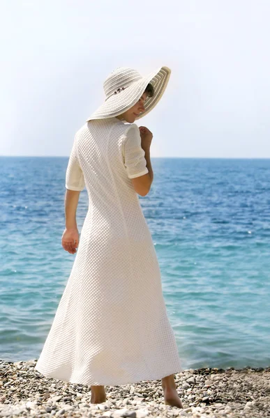 Ung flicka i stor hatt stående på stranden — Stockfoto