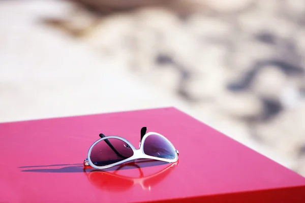 Óculos de sol na mesa vermelha sobre fundo borrado — Fotografia de Stock