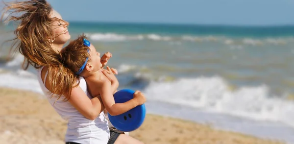 Jovem mãe feliz brincando com o filho no fundo da praia — Fotografia de Stock