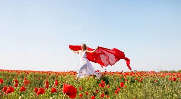 Femme heureuse courir avec écharpe rouge dans le champ de pavot — Photo