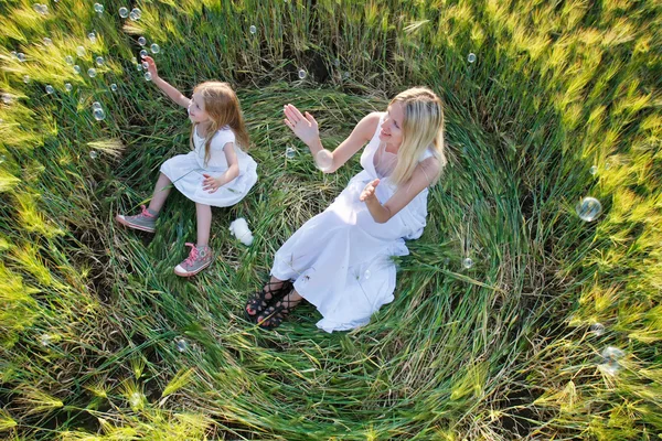 Mother and daughter catching soap bubbles in green field — Stock Photo, Image