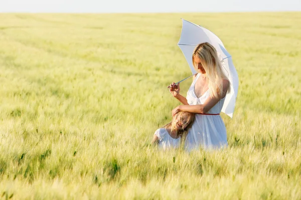 Mãe amorosa e filha sob guarda-chuva branco no campo verde — Fotografia de Stock