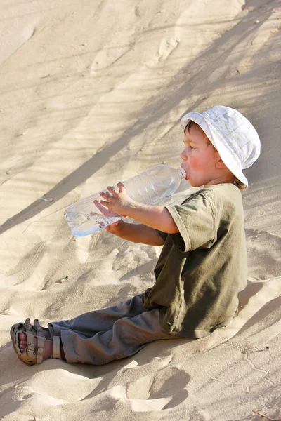 Mladík pitné vody v písku pouště — Stock fotografie