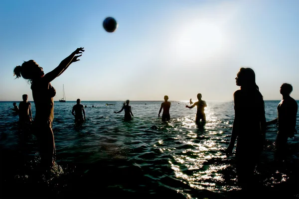 Silhouettes of young playing volleyball in water — Stock Photo, Image