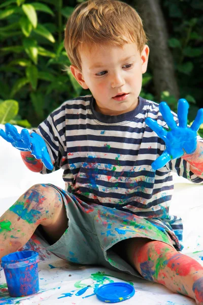 Jongen met zijn handen in blauwe verf buitenshuis — Stockfoto
