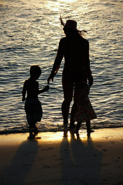 Silhuetas de mãe e dois filhos no pôr do sol fundo do mar — Fotografia de Stock