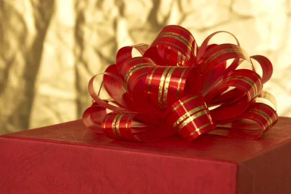 Red ribbon and gift box on gold background — Stock Photo, Image