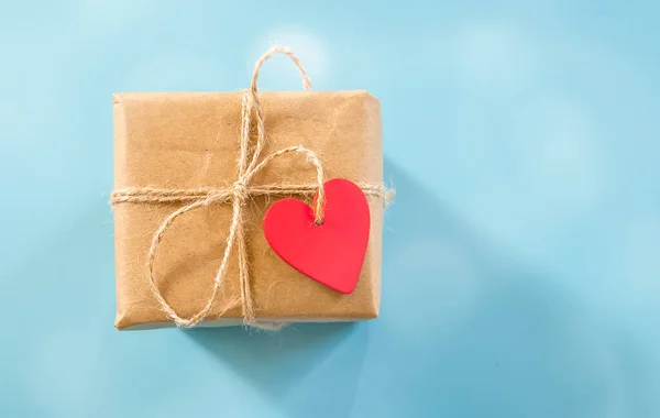 Wrapped gift box with red heart shped tag over blue background, space for text, ad, promo, holidays greeting and celebration concept — Stock Photo, Image