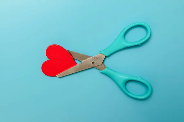 Red wooden heart shape cut with scissors over blue background, conept of sadness, divorce, separation or broken heart feelings — Stock Photo, Image