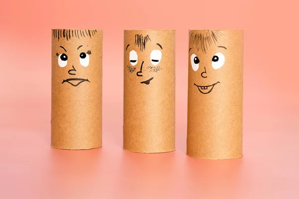 Personajes hechos de rollo de papel higiénico con cara pintada expresando felicidad o satisfacción sobre el fondo rosa, concepto de grupo de emociones, ideas divertidas para la elaboración con niños —  Fotos de Stock