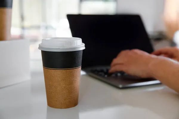 Café en tazas de cartón marrón ordenado y entregado para llevar, entrega de alimentos, comida para llevar, espacio de copia para el texto, persona que trabaja en el ordenador portátil en el fondo — Foto de Stock