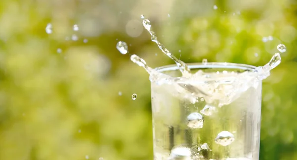 Bicchiere di acqua potabile con bolle, corona di spruzzi d'acqua, sfondo sfocato naturale con luci e ombre. concetto di purezza, acqua potabile, stile di vita sano o medico — Foto Stock