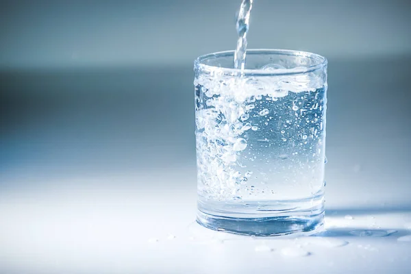 Vaso de agua potable con burbujas, agua está vertiendo, fondo gris estudio con luces y sombras. concepto de pureza, agua potable, estilo de vida saludable o medicina — Foto de Stock