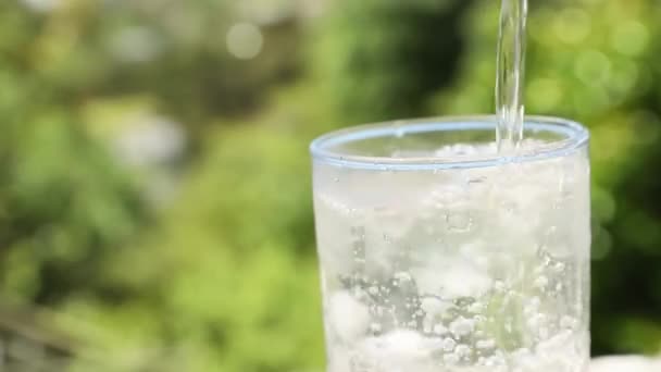 Glass drikkevann med bobler, krone av sprutende vann, naturlig utydelig bakgrunn med lys og skygger. renhetsprinsippet, drikkevann, sunn livsstil eller medisinsk bruk – stockvideo