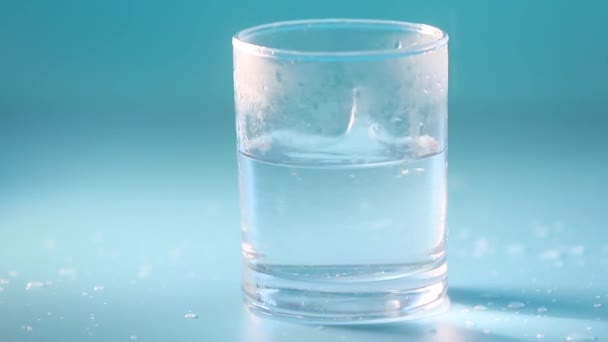 Glas Trinkwasser mit Blasen, Wasser ergießt sich, blauer Studiohintergrund mit Licht und Schatten. Konzept der Reinheit, Trinkwasser, gesunder Lebensstil oder medizinische — Stockvideo