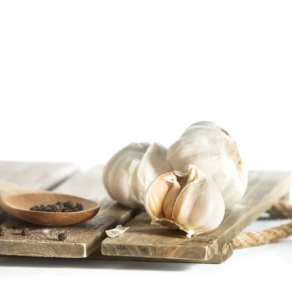 Fresh organic garlic isolated over white background, full heads, cloves and peels, wooden spoon with black pepper, cooking ingredients — Stock Photo, Image