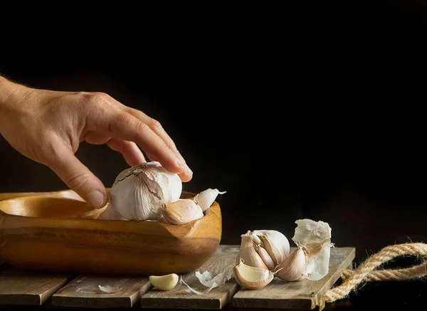 Hand taking fresh organic garlic over black background, full heads, cloves and peels, cooking ingredients — Stock Photo, Image