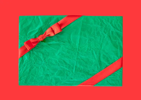 Gift box wrapped in green recycled paper with red ribbon isolated over red background, promo, discount concept, Christmas sales, copy space — Stock Photo, Image