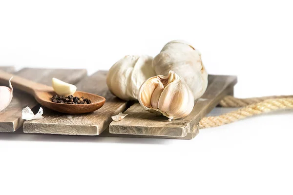 Alho orgânico fresco isolado sobre fundo branco, cabeças cheias, cravos e cascas, colher de madeira com pimenta preta, ingredientes de cozinha — Fotografia de Stock