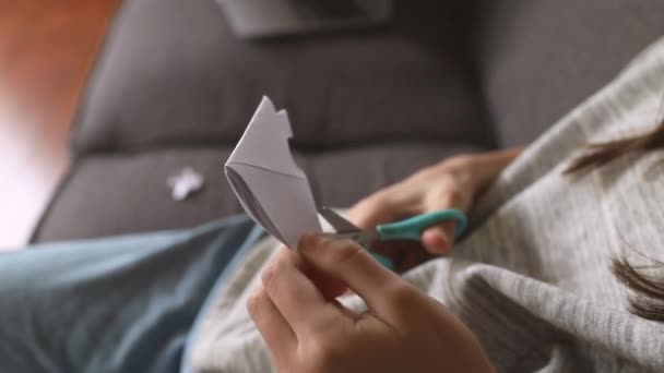 Menina cortando um floco de neve de papel branco com tesoura em casa, educação precoce, artesanato e conceito de arte — Vídeo de Stock